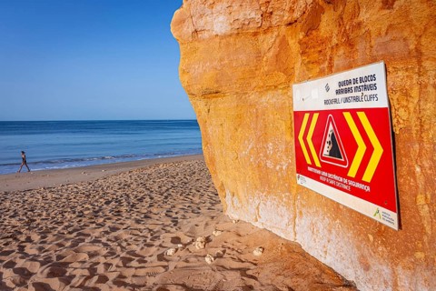 ROCKFALL UNSTABLE CLIFFS, KEEP A SAFE DISTANCE is written in English on a warning sign in Portugal