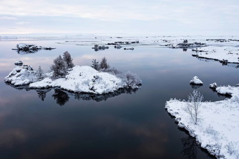 Snow-covered small islands overgrown with bushes in Lake Myvatn, at blue hour, Kalfaströnd, drone