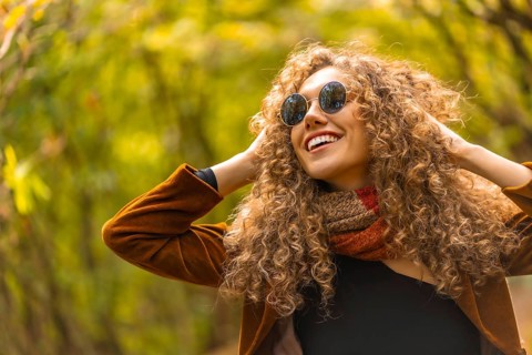 Happy model with curly hair and sunglasses posing and smiling in a park in autumn