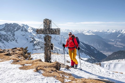 Ski tourers at the summit of the Mitterzeigerkogel with summit cross in winter, Sellraintal,