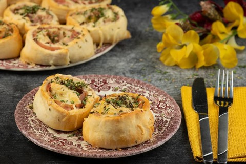 Baked dough snails with sausage and cheese on plates with cutlery and floral decorations in the