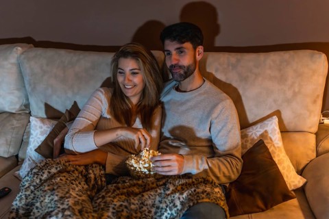 Young couple enjoying a movie night at home, sharing popcorn and relaxing on the sofa under a cozy