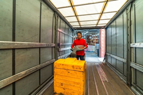 View from inside the vehicle of a male latin warehouse worker loading a truck using hydraulic hand