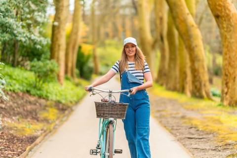 Stylish blonde woman walking with her bicycle on a scenic path, enjoying a leisurely stroll amidst