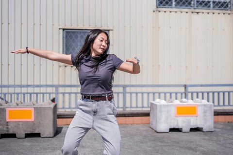 Female young asian K-pop dancer moving energetically in an industrial city space under the sun