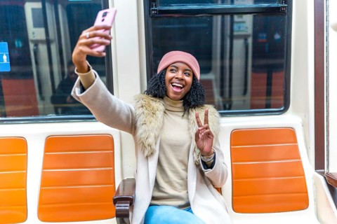 Cheerful young woman smiling and taking a selfie with a peace sign while enjoying her commute on