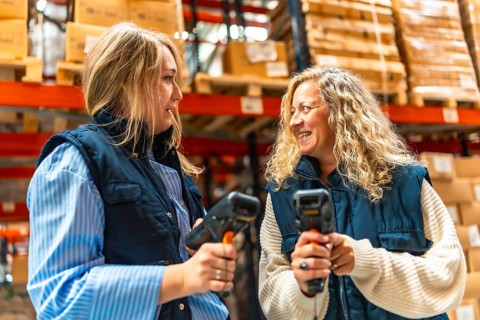 Two female blonde coworkers talking while using barcode scan readers in a distribution warehouse