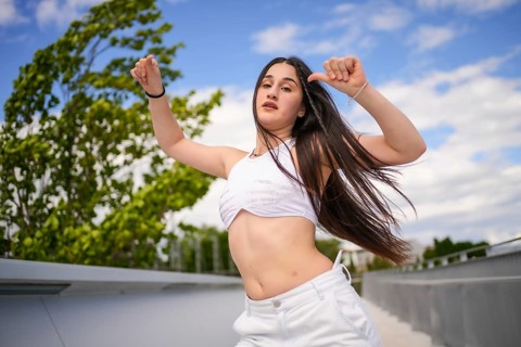 Young caucasian woman with arms raised and tousled hair dancing freestyle on an urban park