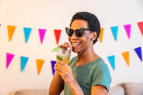 Latin cool man sucking a straw drinking cocktail partying at home