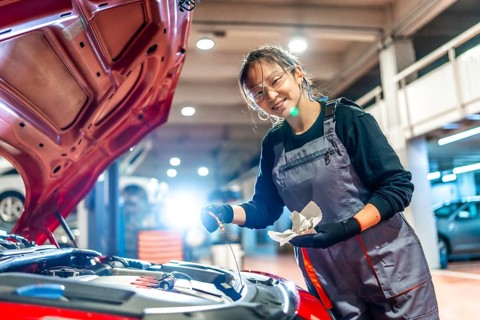Young female mechanic is checking the oil level of a car engine in a garage, holding a dipstick and