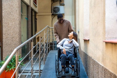 African man helping a disabled work colleague pushing the wheelchair along a ramp next to coworking