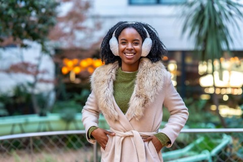 Portrait of a young woman wearing winter clothes and earmuffs smiling in urban city during winter