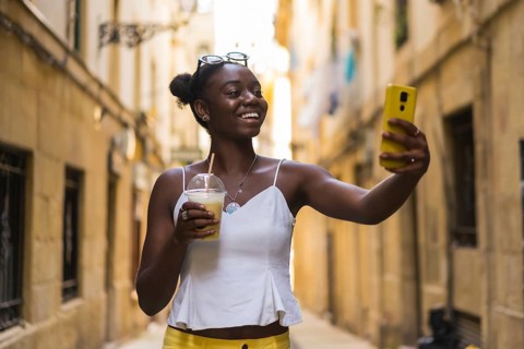 Smiling young african american woman talking selfie showing a delicious milkshake in the city