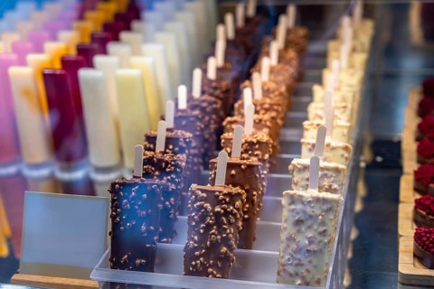Delicious ice cream popsicles with chocolate and nuts coating displayed in rows in a shop window