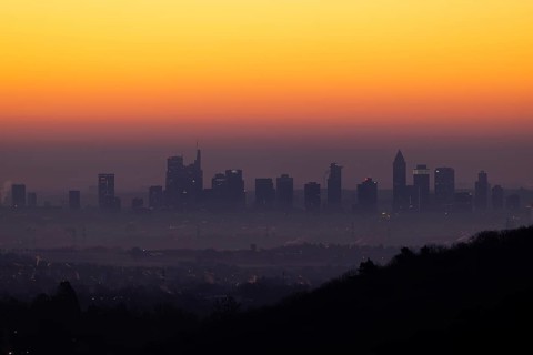Shortly in front of sunrise, the sky behind the Frankfurt banking skyline turns yellow and orange,