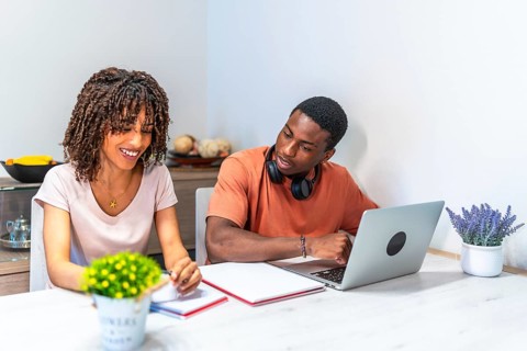 Young black entrepreneurs working from home using laptop and taking notes, collaborating on a