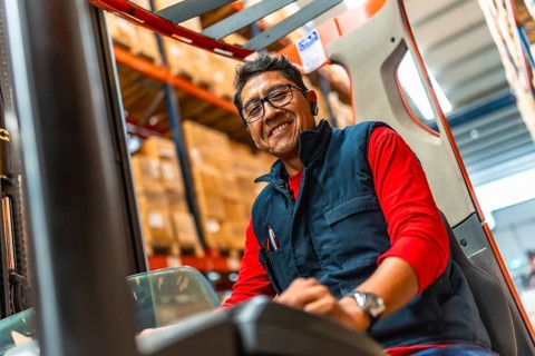 Close-up photo of a happy latin man worker driving forklift in a warehouse