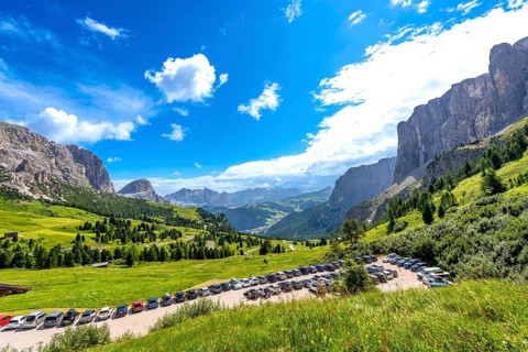 Cars parked near gardena pass with breathtaking views of the dolomites mountains in a sunny summer