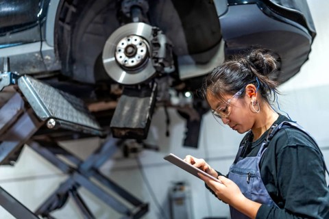 Young female mechanic using a digital tablet while inspecting a car raised on a hydraulic lift in a