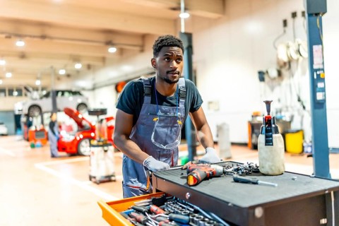 Young african car mechanic pushing a tool trolley in a busy workshop, preparing to repair a car