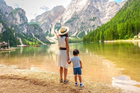 Mother pointing at the landscape while holding her son's hand on the shore of lake braies in the