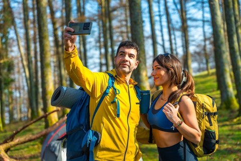 Couple taking a selfie with smartphone in the woods during camping trip, wearing backpacks and