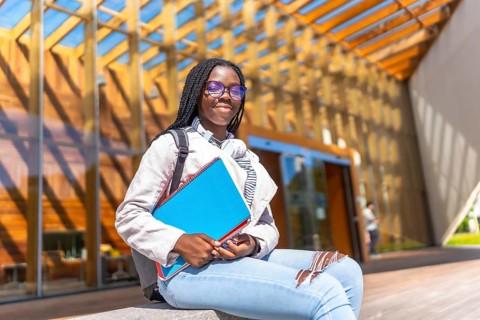 Female african student sitting outside the university and smiling at camera in a sunny day