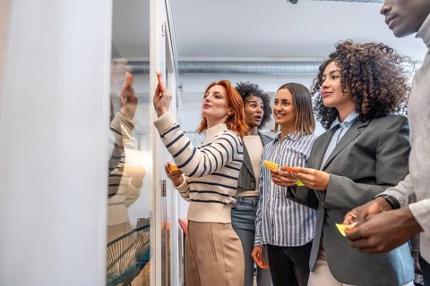 Side view of people participating in a creative process in a coworking using sticky notes on glass