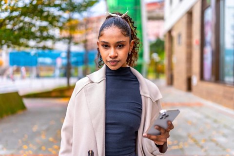 Portrait of a beauty african american woman looking at camera, using phone outdoors in the city