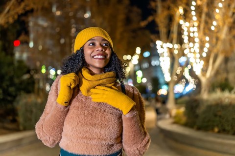 Smiling woman wearing winter clothes enjoying christmas lights decorating city trees at night