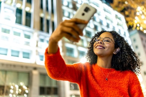 Smiling woman capturing a selfie with her mobile phone in a vibrant urban city, surrounded by