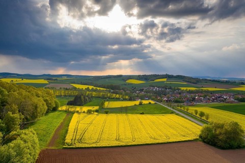 View of Tiftlingerode between blooming rape fields in rain and sunshine, Duderstadt, Lower Saxony,