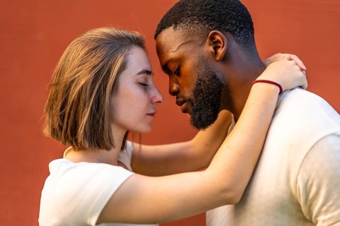 Multi-ethnic couple showing affection and hugging each other against red urban wall