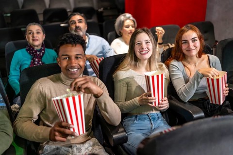 Multi ethnic group of friends enjoying a film at the movie theater, sharing laughter and munching