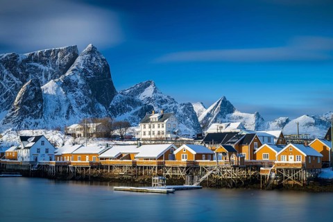 Traditional yellow rorbuer huts on the island of Sakrisøy, snow-capped mountains in the background,
