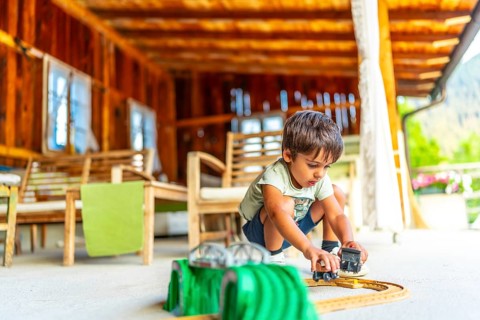 Child engaging with toy cars on a sunny outdoor porch surrounded by wooden furniture