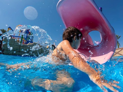 Child having fun swimming through inflatable ring in water park during summer vacation, enjoying