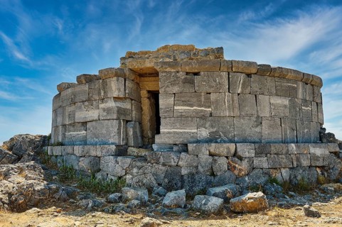 Ancient stone tower in ruins, surrounded by large rocks and blue sky, tomb of Cleovoulos the