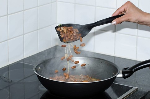 Woman Hand Holding and Using a Big Spoon to Cooking Beans with a Frying Pan in Kitchen in