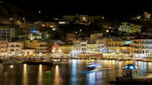 Night shot of a harbour with illuminated buildings and reflecting lights in the water, Pigadia,