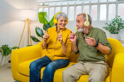 Cute senior couple listening to music together and dancing sitting on the sofa indoors