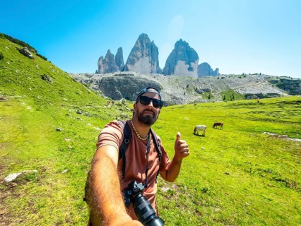 Photographer taking a selfie with thumbs up sign while hiking on a trail in tre cime di lavaredo,