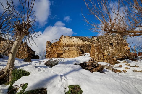 Snow-covered, abandoned ruin under a blue sky with bare trees in winter, village, Zourva, Lefka
