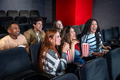 Group of young people enjoying a movie at the cinema, sharing laughter and smiles while munching on