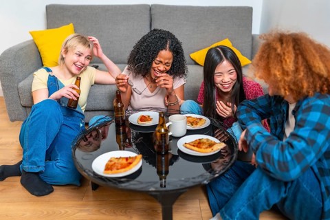Four female friends sharing a meal of pizza and beer, laughing and having fun together in their