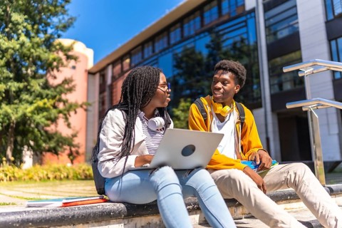 Two african american students using laptop sitting on the campus