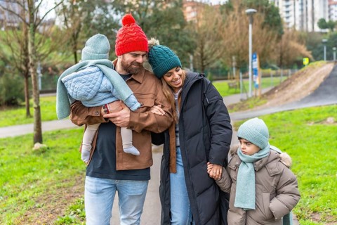 Smiling parents walking with their children in a park on a chilly winter day, enjoying moments of