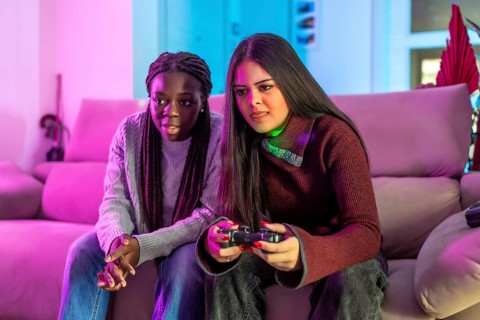 Two female friends enjoying their free time playing video games together on the sofa at home