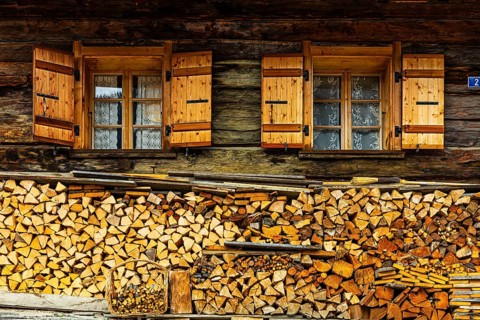 Old windows with shutters on an old farmhouse, firewood piled up in front, mountain village of
