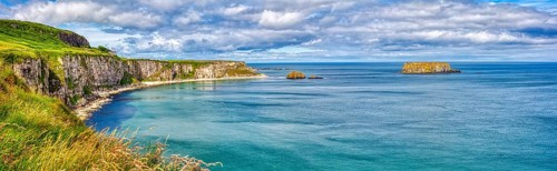 Long coastline with steep cliffs and calm blue sea under cloudy skies, County Antrim Coast